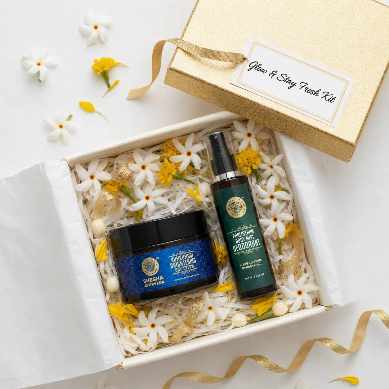 Shesha Ayurveda Glow & Stay Fresh Kit overhead flat lay in gold gift box with Parijatham flowers and marigold petals