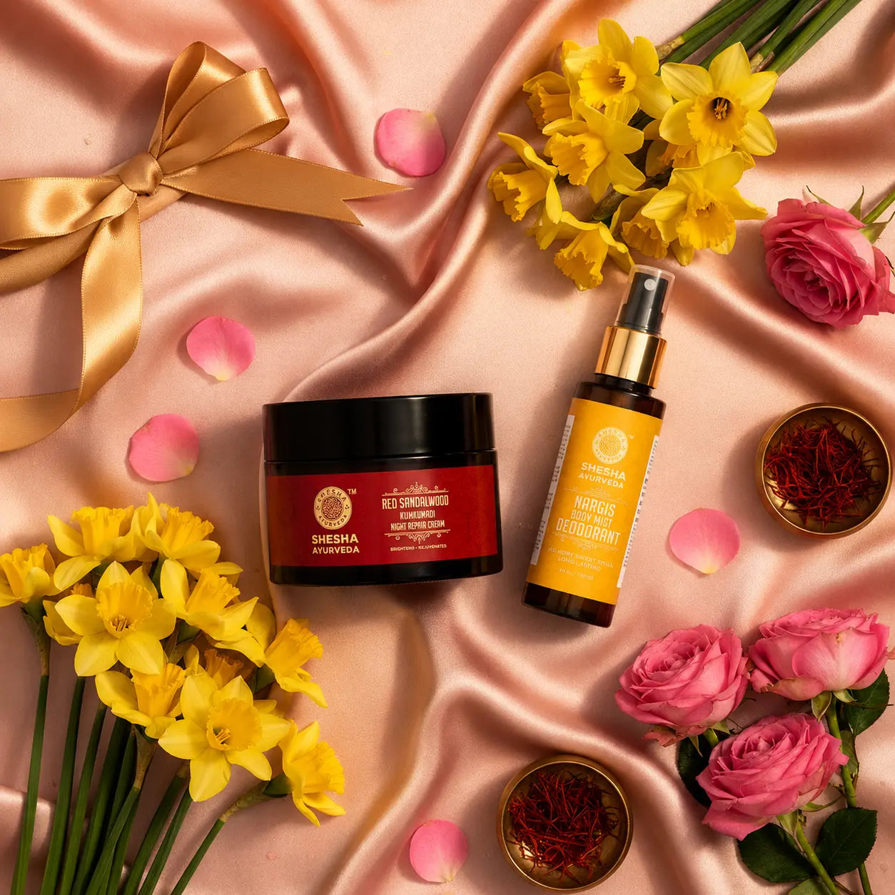 Shesha Ayurveda Bloom & Glow Kit Mother's Day gift flat lay with pink silk, Nargis flowers and roses